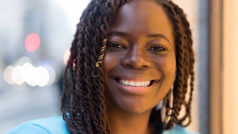 Pretty young black woman in the middle of the city, smiling at camera. Selective focus.