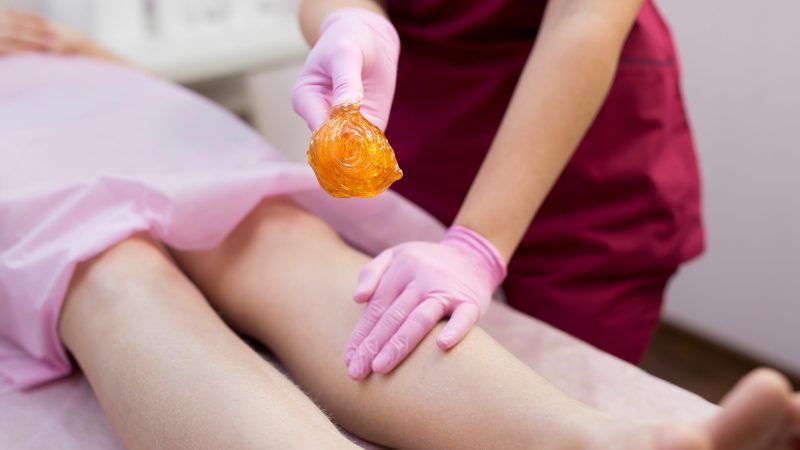 Sugar depilation of the feet in the beauty salon. Rid of hair on the legs. Sugaring. Master shugaring applies thick sugar paste on the legs of a young girl, removing hair on the legs. Close-up.